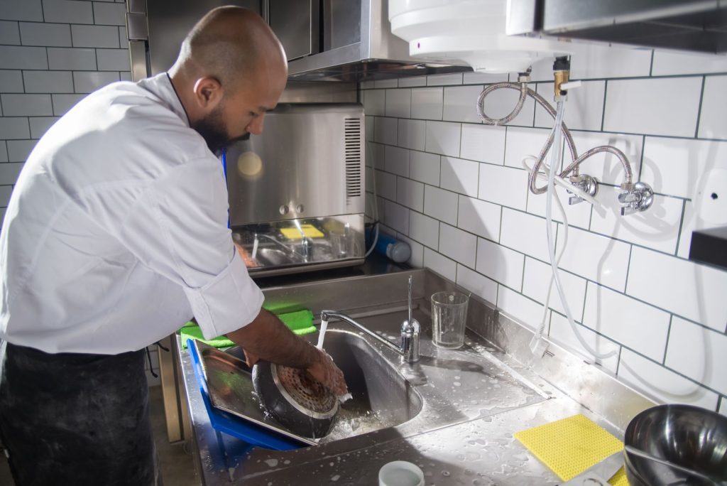 Chef washing up at a stainless steel commercial kitchen sink