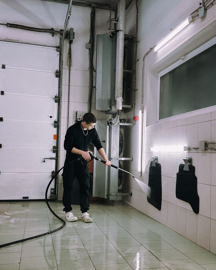 Worker using a high-pressure water jet to clean a facility floor and drain