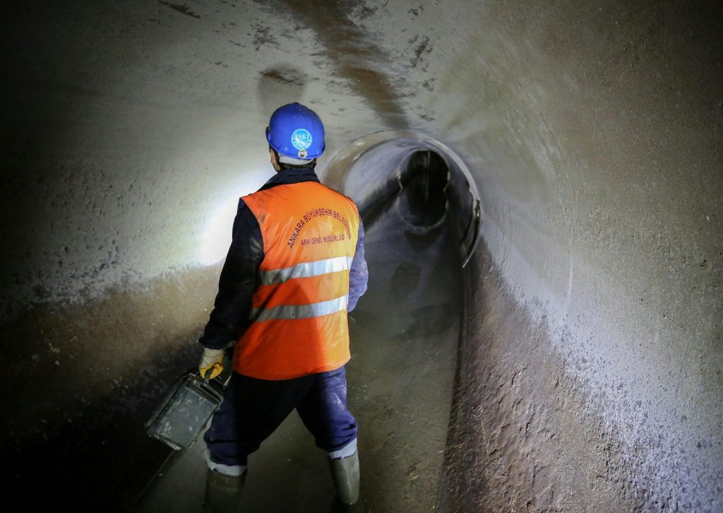 Worker in safety gear walking through a sewer tunnel